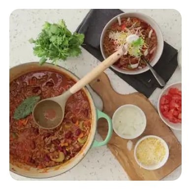 A bowl of chili served from a pot with toppings on the side