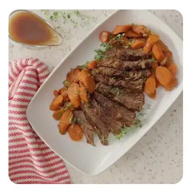 A white serving dish with sliced brisket, carrots and gravy A white serving dish with sliced brisket, carrots and gravy