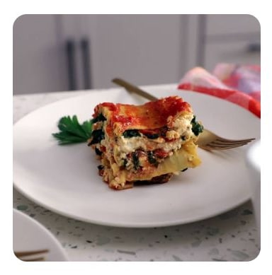 A slice of vegan lasagna and a fork on a white plate