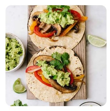 Two fajitas with guacamole and vegetables on a wooden cutting board