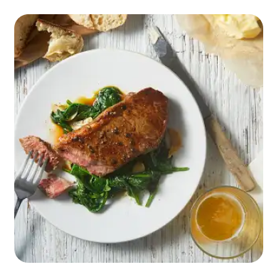A plate of medium rare steak over cooked spinach