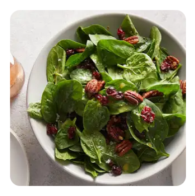 A bowl of spinach salad with walnuts and dried cranberries