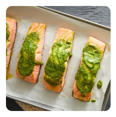 Salmon filets on a baking sheet topped with green pesto spread Salmon filets on a baking sheet topped with green pesto spread