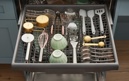 A dishwasher third rack loaded with utensils, small bowls and spoons