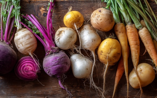 A selection of root vegetables, including carrots, on a wood background