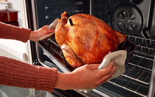 Someone pulling a crispy, golden turkey out of an oven