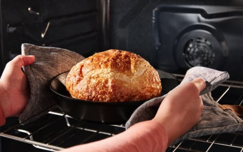 A person pulling fresh bread out of an oven