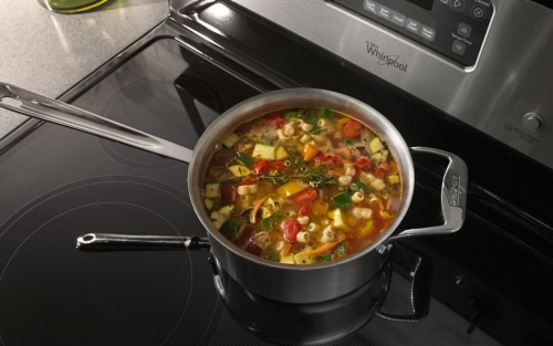 A stew of vegetables, herbs and pasta cooking on a burner