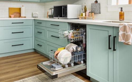 Open dishwasher filled with clean dishes between light blue cabinets