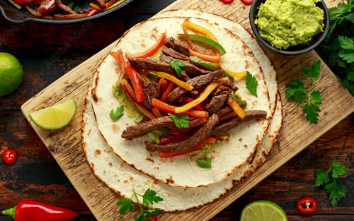 Flank steak fajita with bell peppers and tortilla on a wood serving board