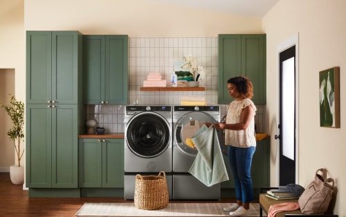 Person folding laundry in front of Whirlpool® Washer and Dryer pair on pedestals