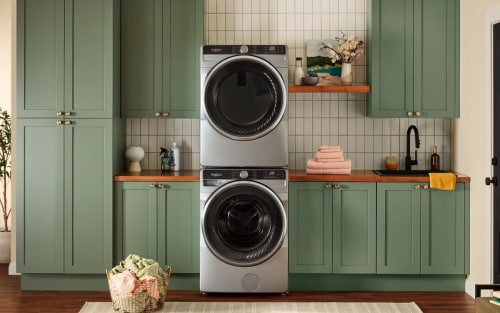A stainless steel stackable washer and dryer in a laundry room with green cabinetry