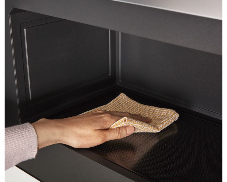 Quelqu'un essuie l'intérieur d'un four à micro-ondes encastré Whirlpool