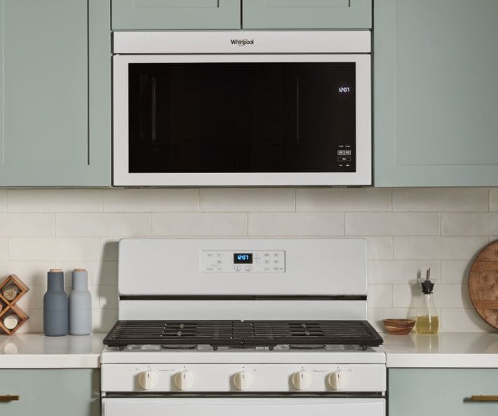 Un four Whirlpool situé sous un four à micro-ondes encastré. Sur le plan de travail se trouvent des salières et poivrières, un porte-épices, un contenant d'huile et une planche à découper