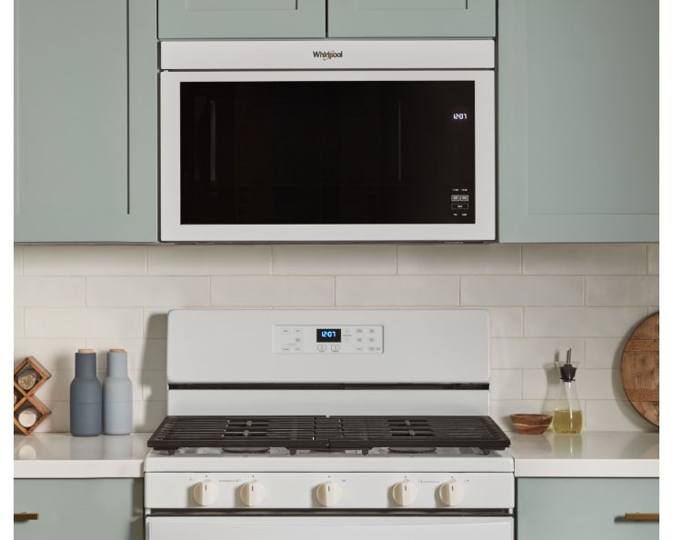 Un four Whirlpool situé sous un four à micro-ondes encastré. Sur le plan de travail se trouvent des salières et poivrières, un porte-épices, un contenant d'huile et une planche à découper