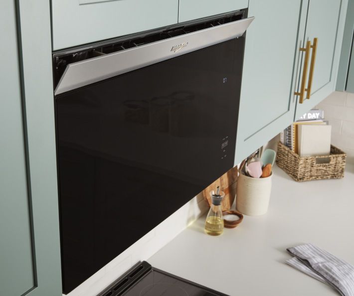 Un four à micro-ondes encastré Whirlpool intégré. Sur le comptoir se trouve un porte-ustensiles de cuisine, un contenant d'huile, un petit plat de sel et un panier de livres de cuisine