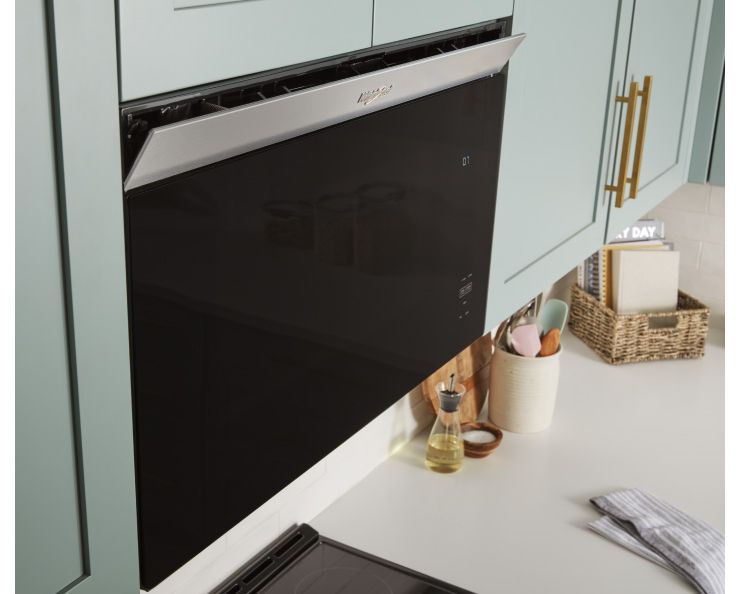 Un four à micro-ondes encastré Whirlpool intégré. Sur le comptoir se trouve un porte-ustensiles de cuisine, un contenant d'huile, un petit plat de sel et un panier de livres de cuisine