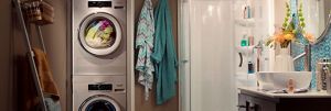 Une salle de lavage avec une serviette suspendue à une échelle et deux peignoirs suspendus. Il y a une laveuse Whirlpool avec des vêtements en train d'être lavés
