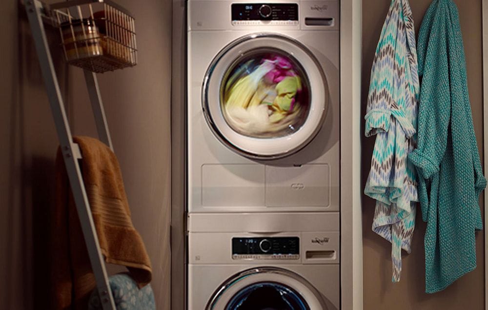 A laundry room with a towel hanging on a rank and two hanging bathrobes. There's a Whirlpool Washing Machine with clothes in the middle of being washed
