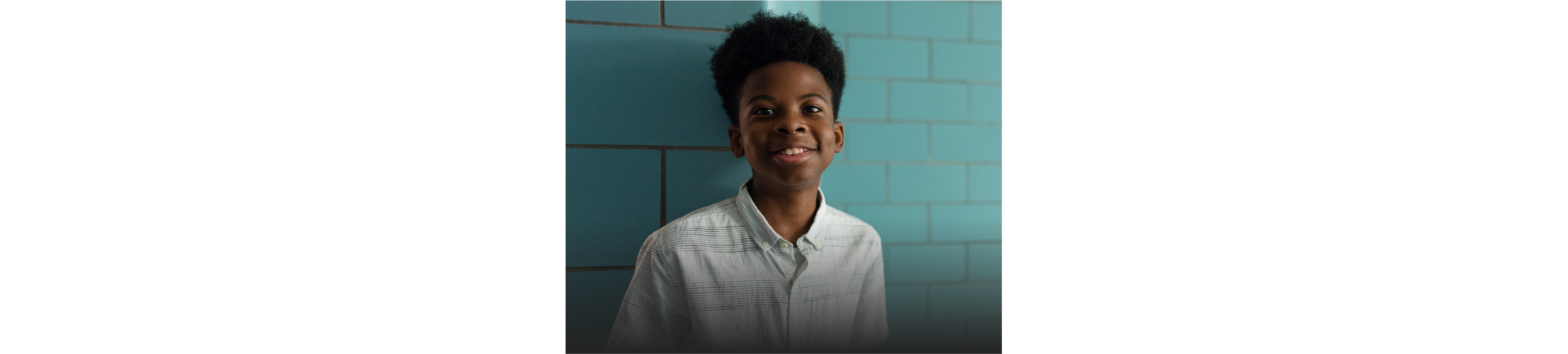 A smiling child stands against a blue-green wall