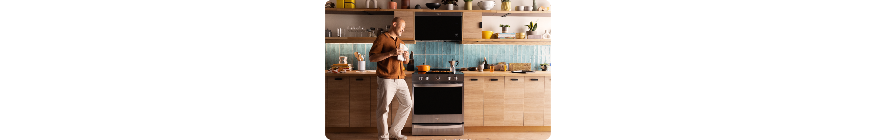 A person walking through a modern kitchen with light wood cabinets and Whirlpool brand appliances