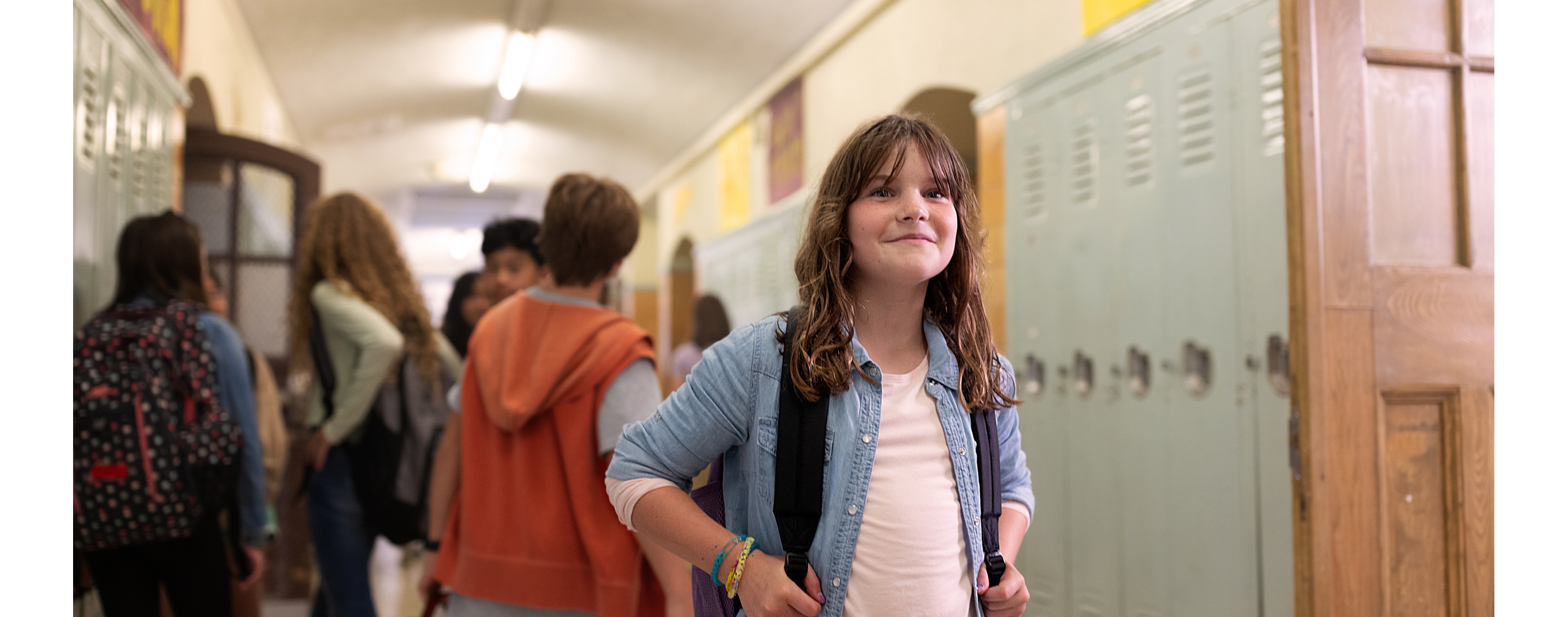 A smiling child in a school hallway with other kids behind them