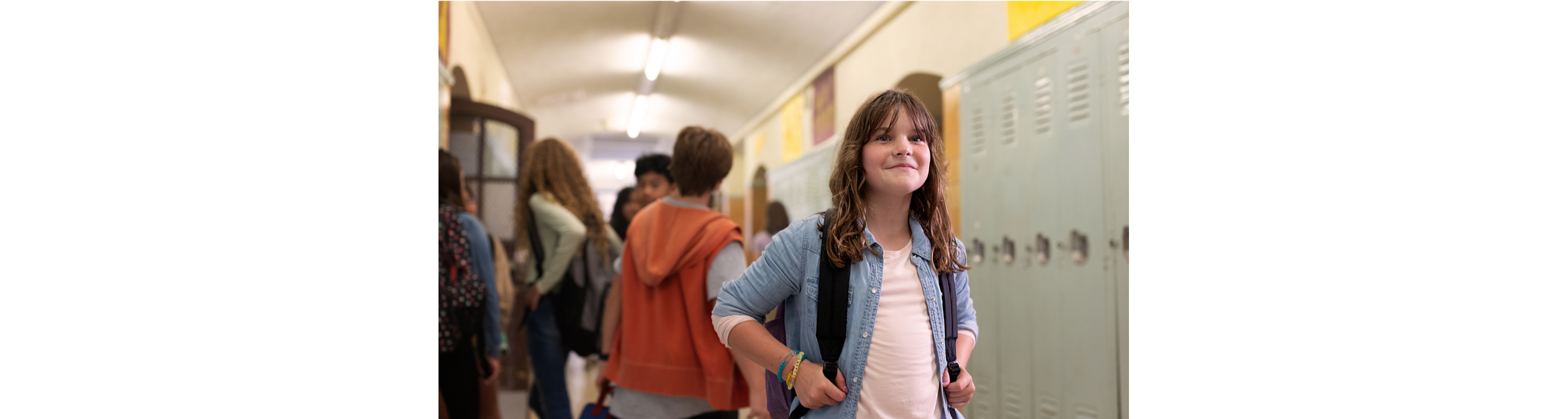 A smiling child in a school hallway with other kids behind them