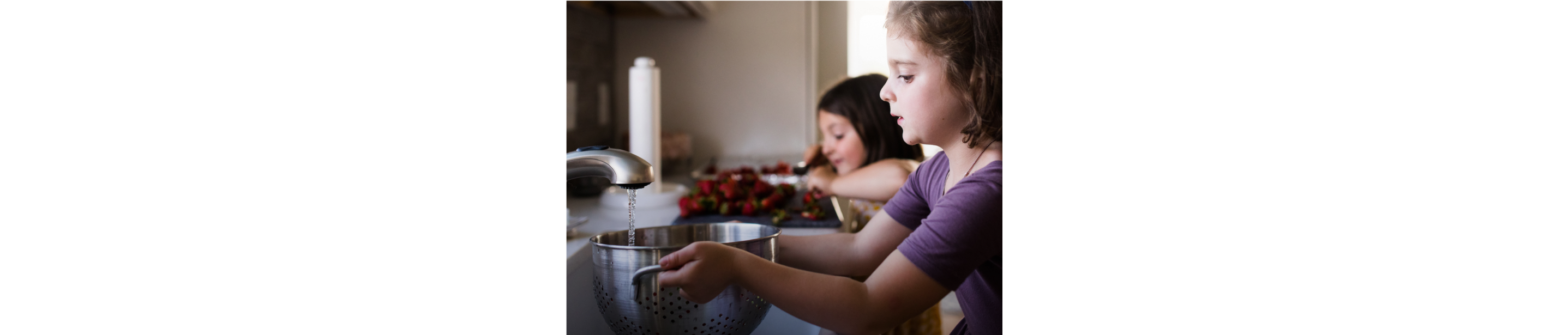Two children rinsing fruit in a sink
