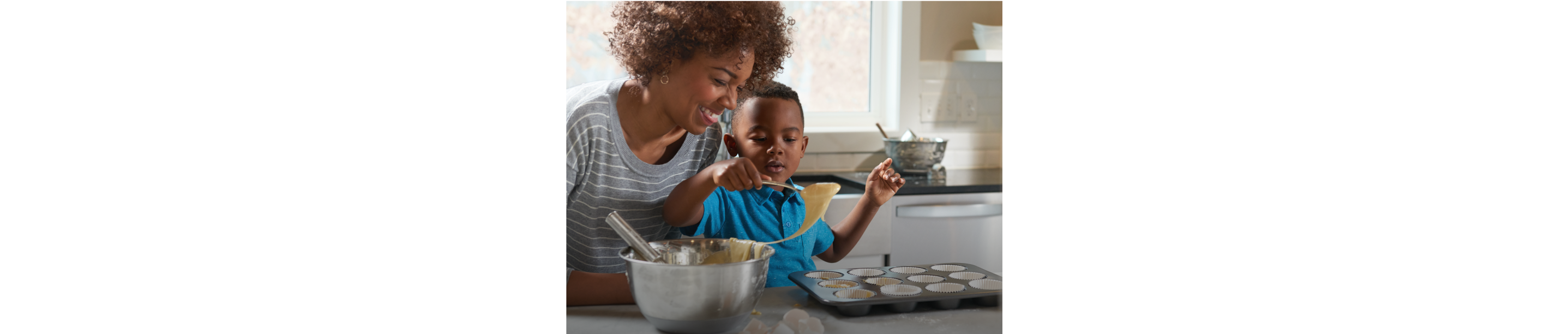 An adult and a child fill a cupcake tin with batter