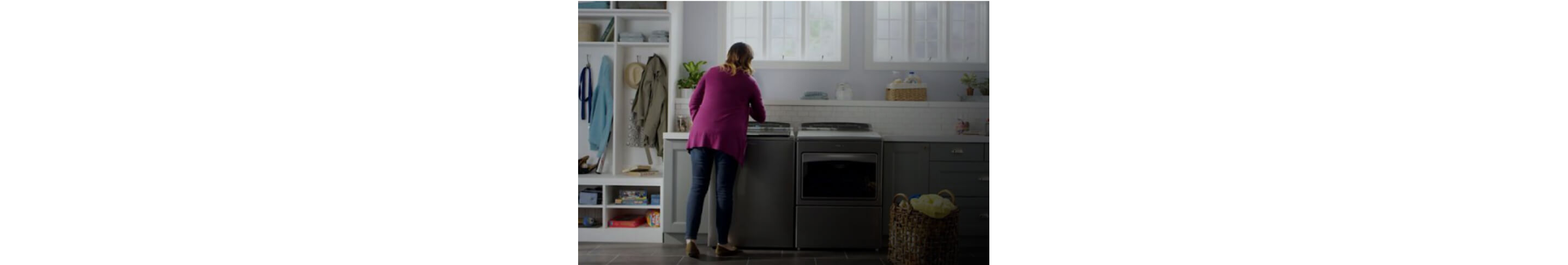 A person interacting with a Whirlpool® Top Load Washer and Dryer in a laundry room
