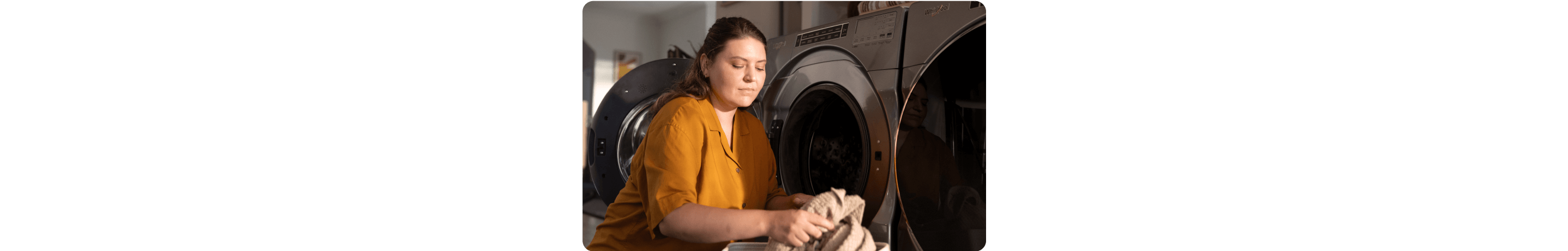 A person in a yellow blouse loading a dark gray washing machine at home