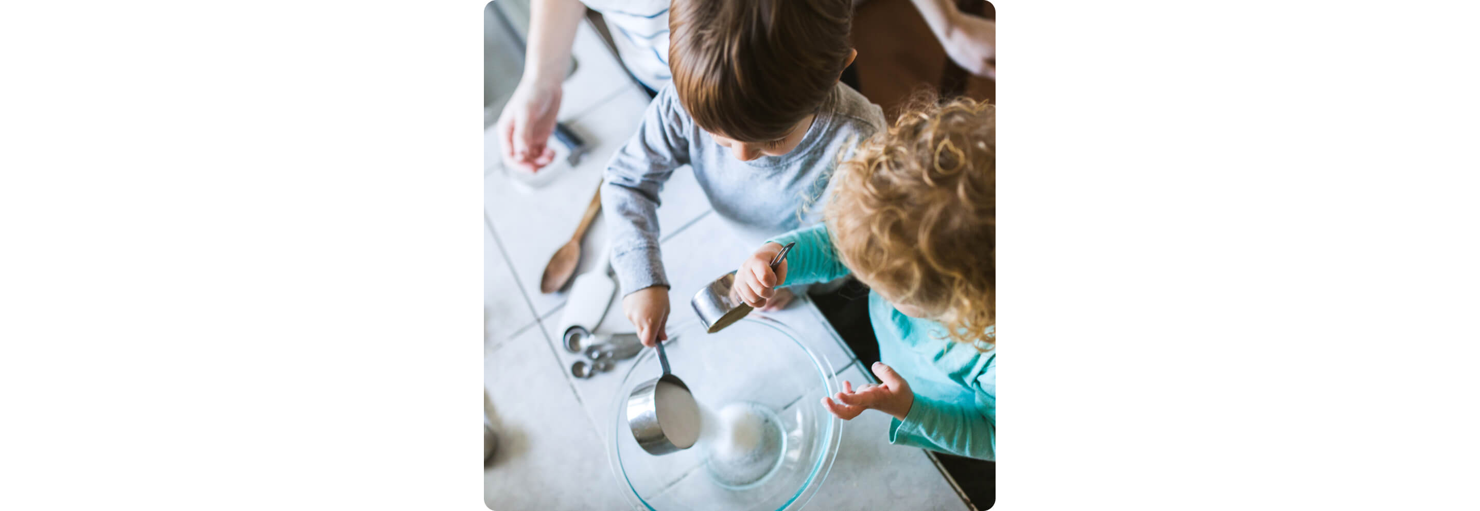 Young children pouring baking ingredients into a glass bowl