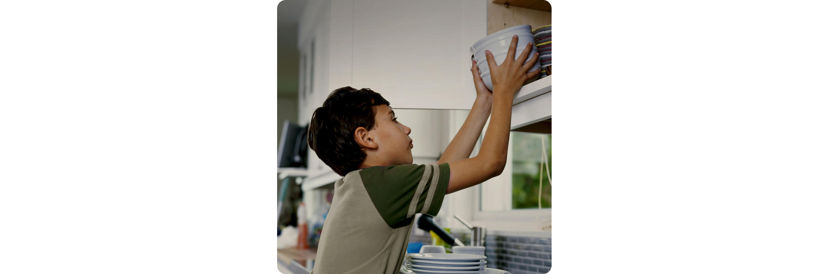 A young boy putting away a stack of bowls in the cabinet