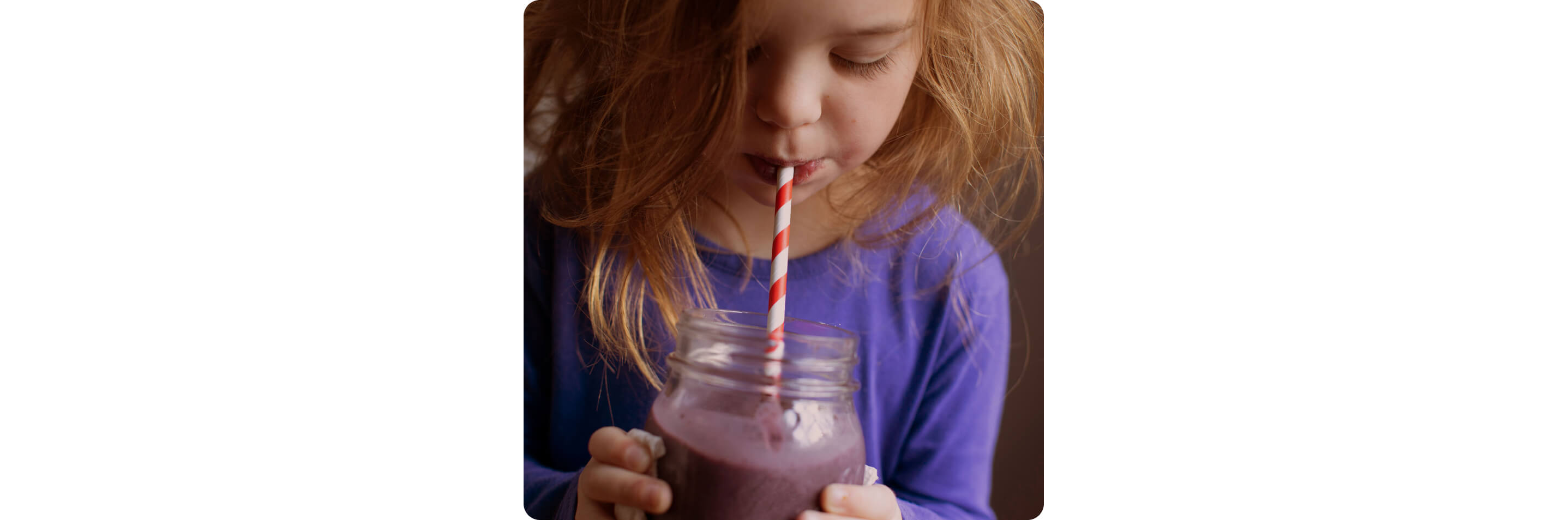 A child drinking a smoothie from a mason jar