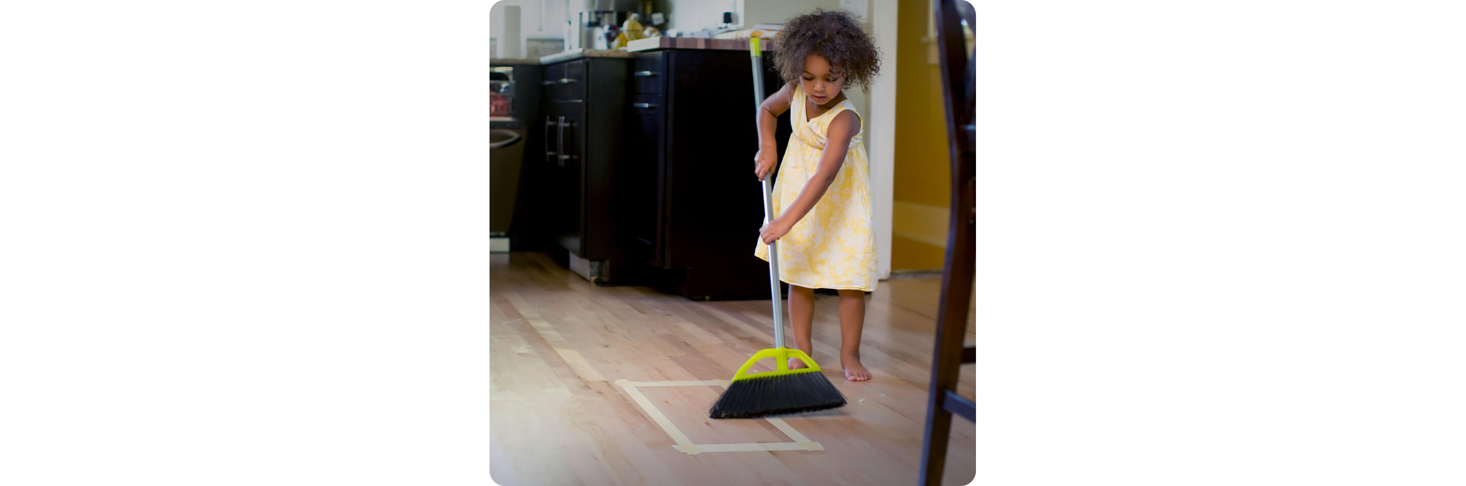 A girl sweeping crumbs into a taped square on the floor