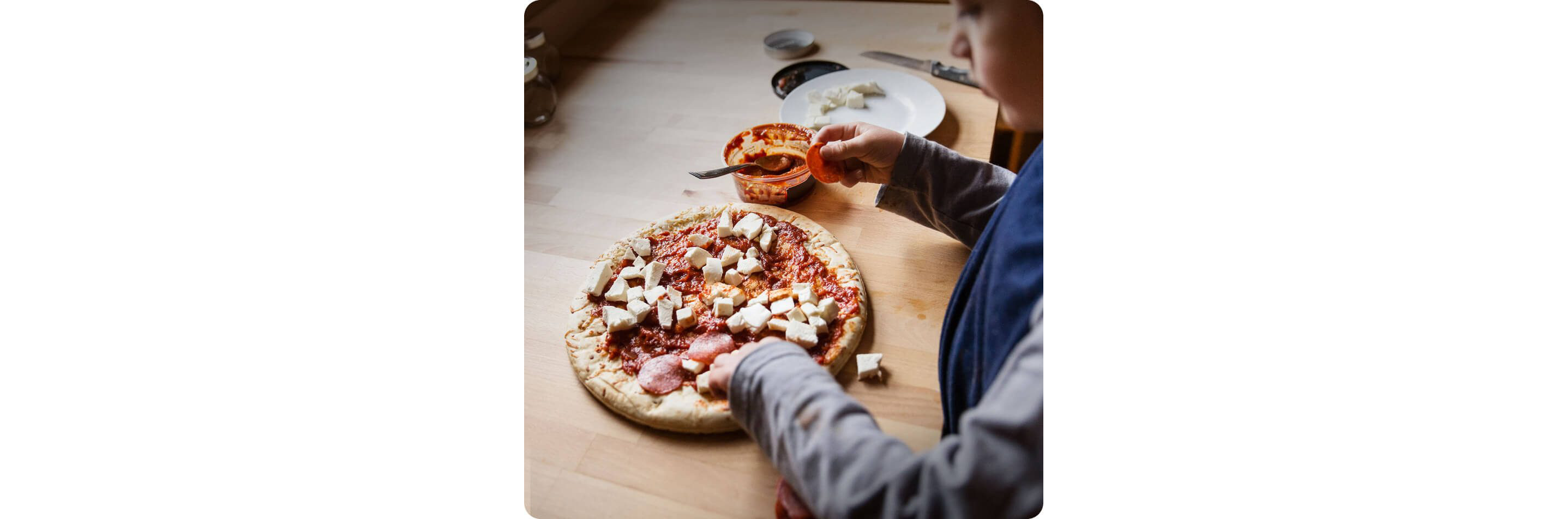 A child topping a pizza with cheese and pepperoni