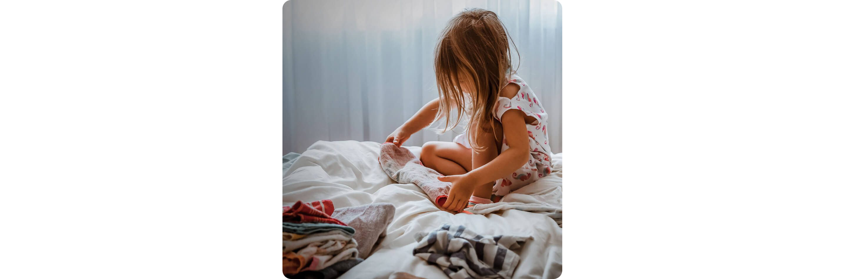 A child sitting on a bed while folding small towels