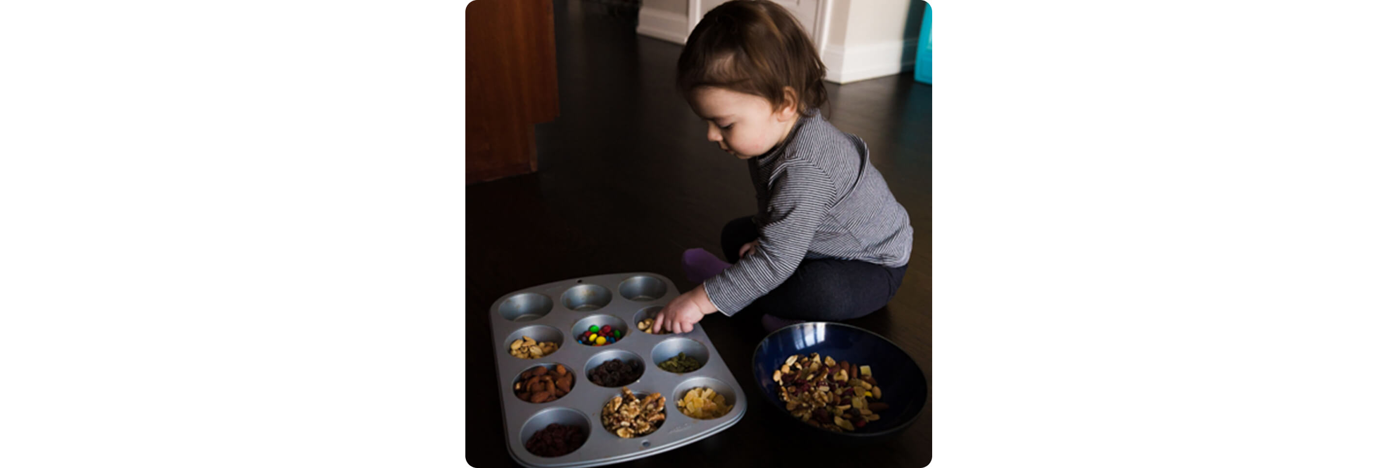 A toddler sorting trail mix in a muffin tin