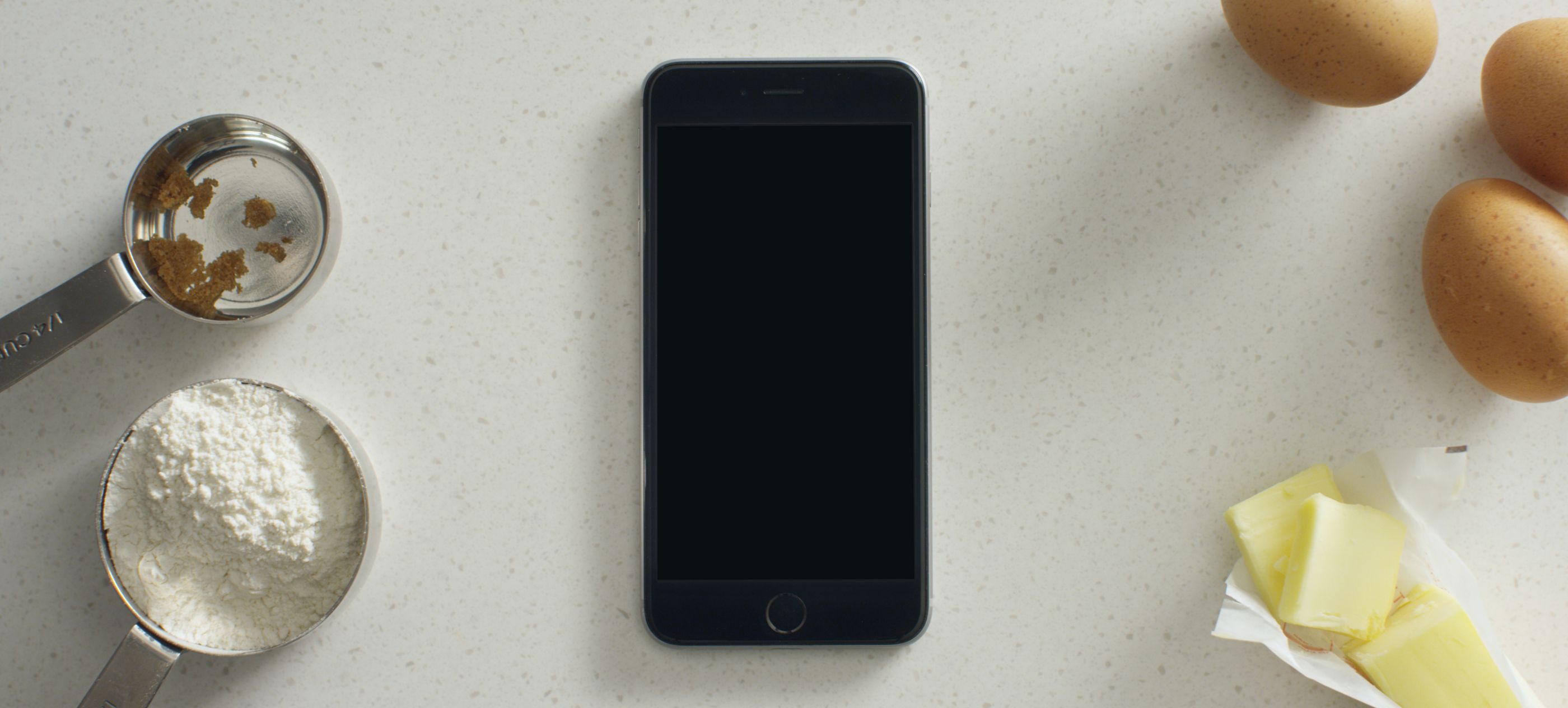 A smart phone with the Whirlpool app on the screen, sitting on a countertop surrounded by baking supplies.