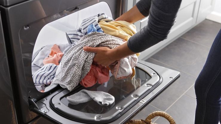 A person loads clothes into a dryer.