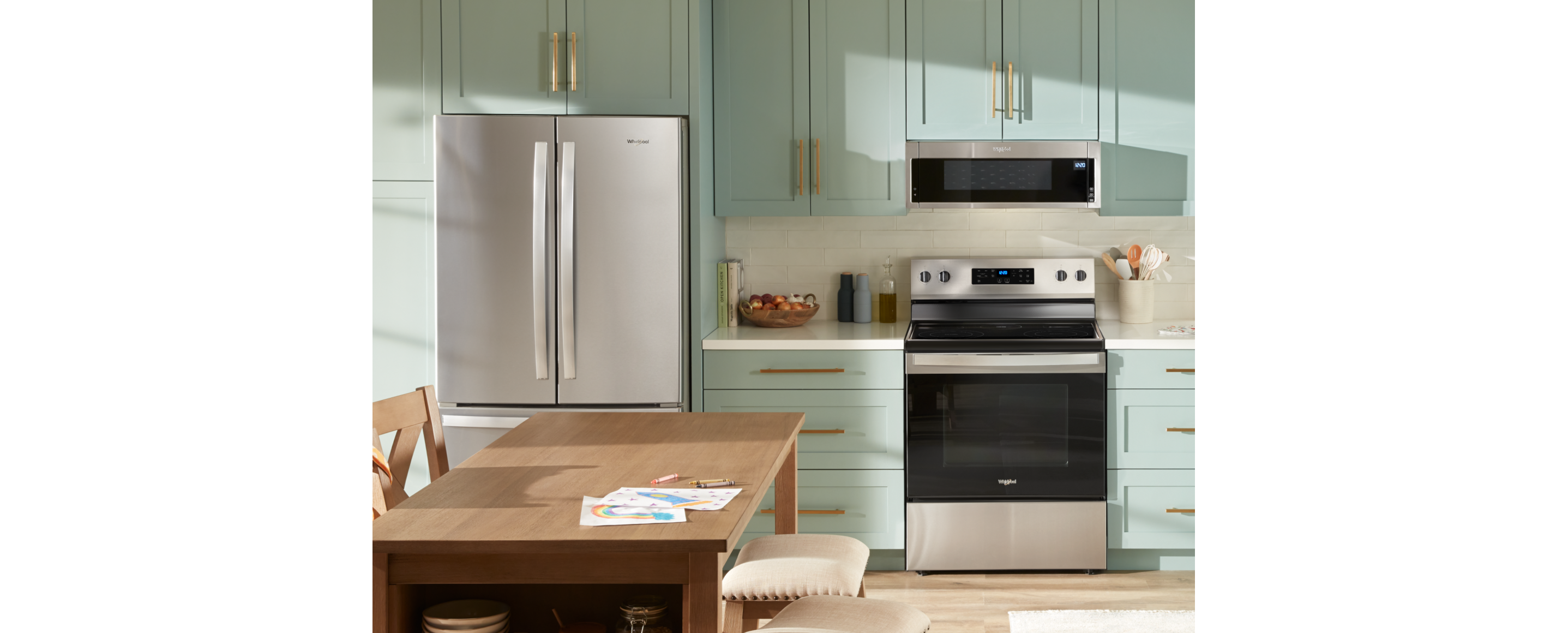 A suite of Whirlpool® appliances in a kitchen with light green cabinets and a wood kitchen island