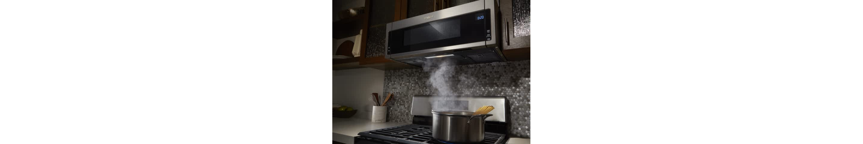 A steaming pot sits on the stove beneath a Whirlpool® Low Profile Over-The-Range Microwave