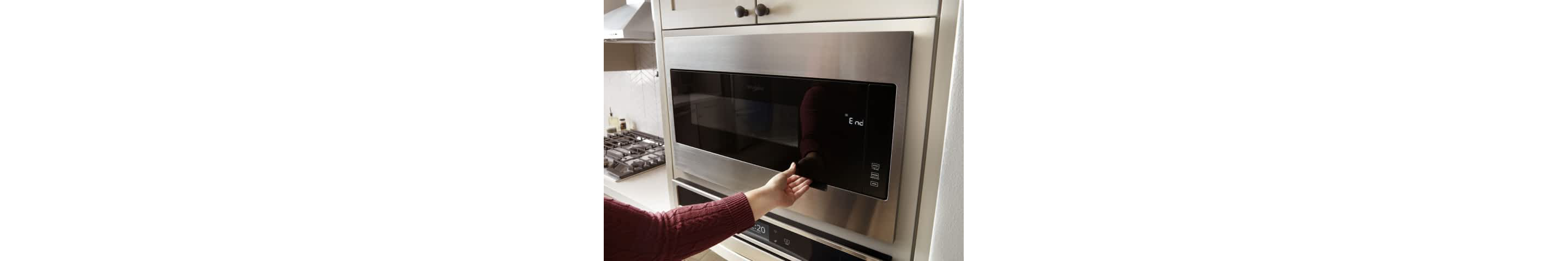 An arm reaches for the handle of a Whirlpool® Built-In Microwave