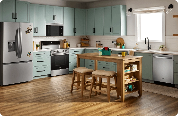 A bright kitchen with blue-green cabinets and a suite of stainless steel Whirlpool® Appliances