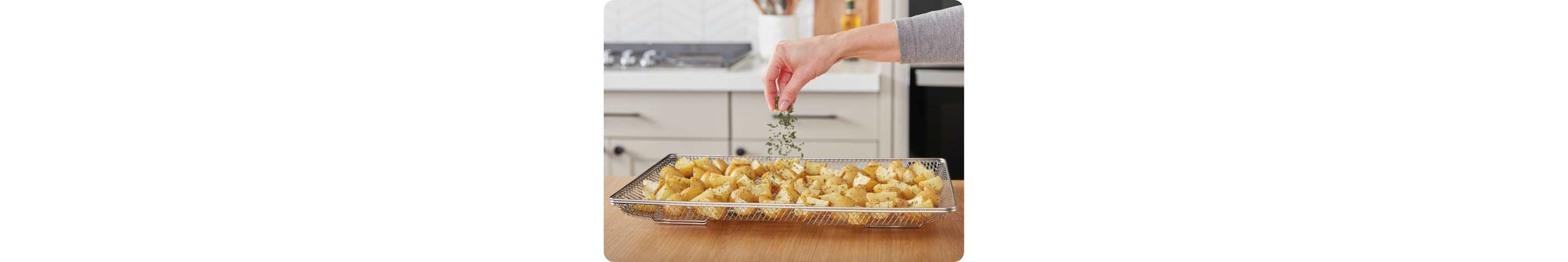 A hand sprinkling herbs onto air fried potatoes in an air fry basket