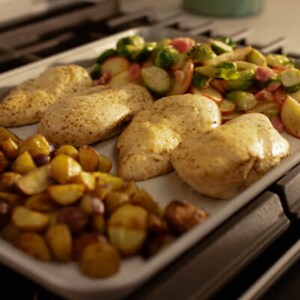 Chicken, veggies and potatoes on a sheet pan on a cooktop