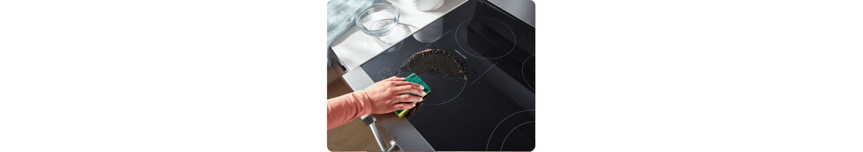 Person wiping baked-on foods from the cooktop with a sponge.