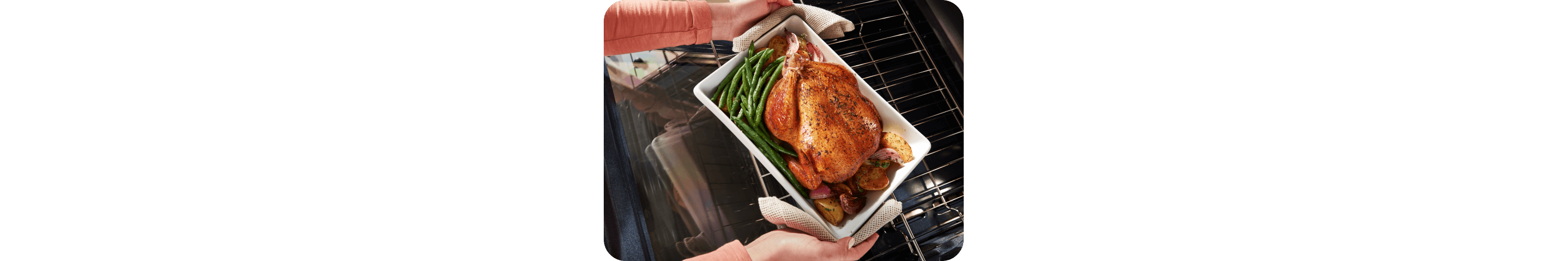 Person pulling a roasted chicken and vegetables out of a Whirlpool® Range