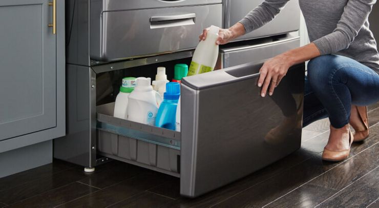 Someone placing a bottle inside the extra storage space of a Whirlpool Laundry Appliance. Inside the drawer are bottles of detergent and cleaner