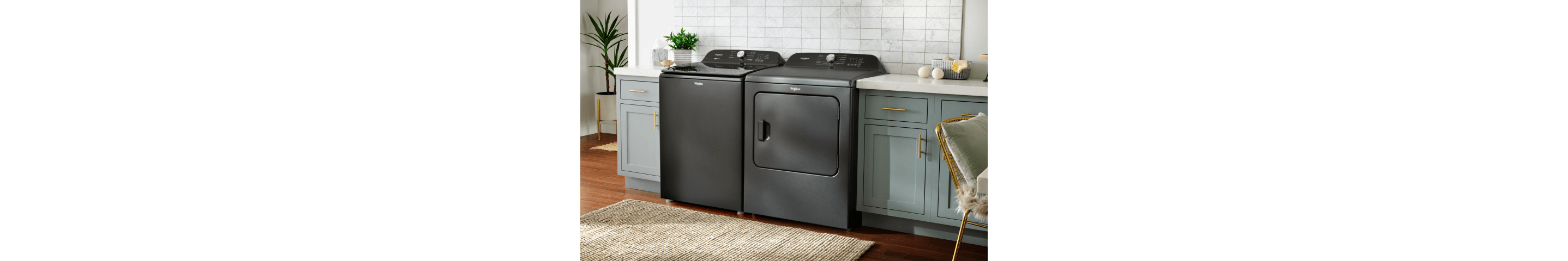 A Volcano Black top load Whirlpool® Washer and Dryer in a laundry room with light cabinets